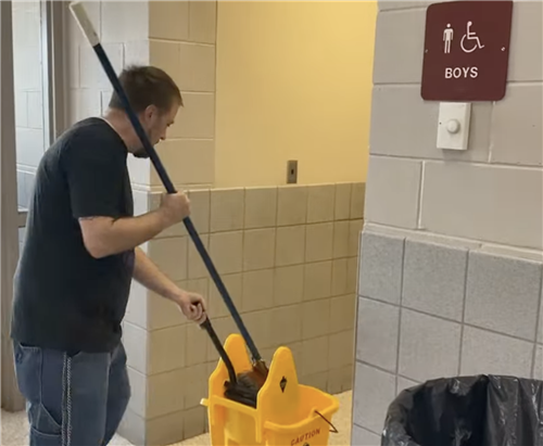custodian with yellow bucket cleaning boys restroom